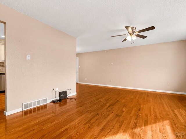 unfurnished living room with visible vents, a ceiling fan, a textured ceiling, wood finished floors, and baseboards