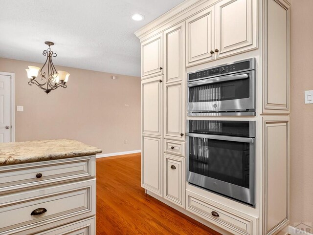 kitchen with pendant lighting, stainless steel double oven, light stone countertops, light wood-type flooring, and baseboards