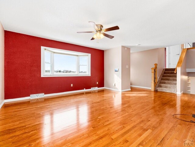 unfurnished living room with light wood-style floors, baseboards, stairway, and visible vents