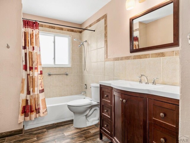 bathroom featuring toilet, shower / tub combo, wood finished floors, vanity, and tile walls