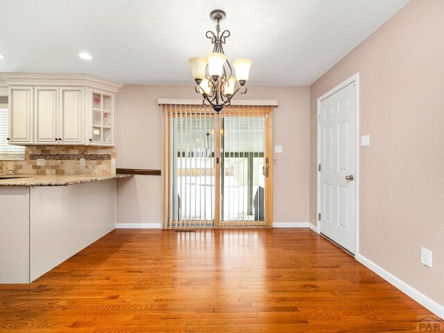 unfurnished dining area featuring a chandelier, light wood-style flooring, and baseboards