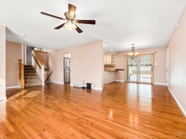 unfurnished living room featuring light wood-style floors, visible vents, stairway, and baseboards