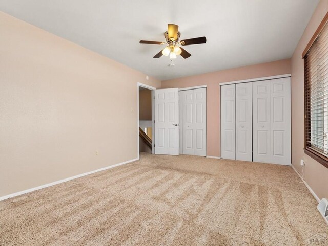 unfurnished bedroom featuring a ceiling fan, carpet flooring, baseboards, and two closets