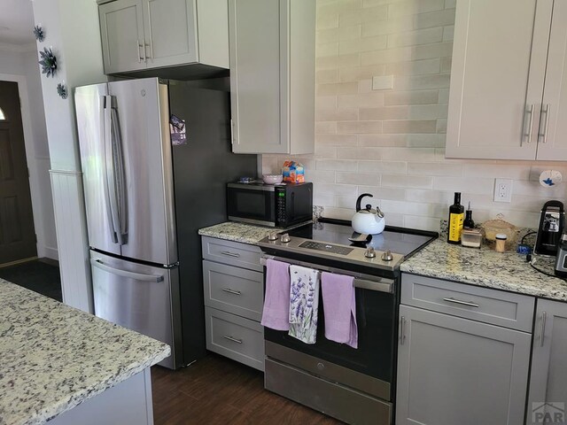 kitchen with dark wood-style floors, stainless steel appliances, light stone counters, and gray cabinetry