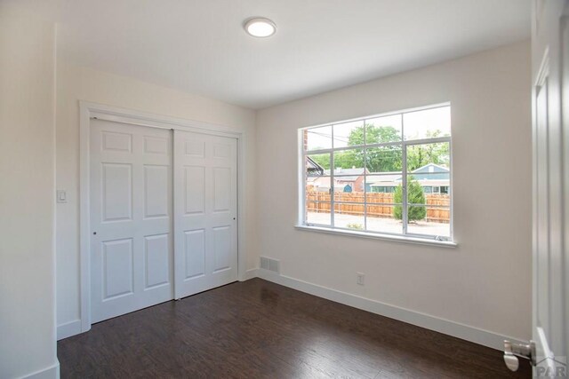 unfurnished bedroom featuring visible vents, a closet, baseboards, and dark wood-type flooring