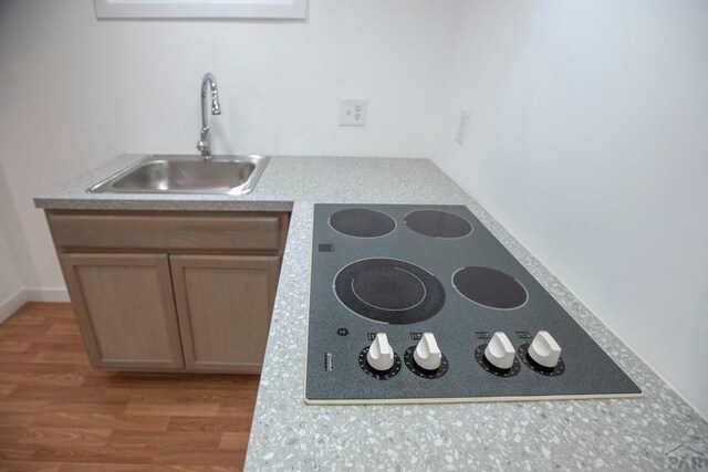 kitchen with black electric stovetop, light countertops, brown cabinetry, a sink, and wood finished floors