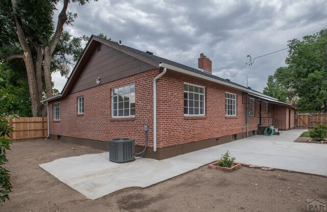 exterior space with a patio, central air condition unit, brick siding, fence, and a chimney