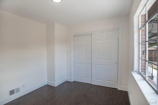 unfurnished bedroom featuring a closet, dark wood finished floors, visible vents, and baseboards