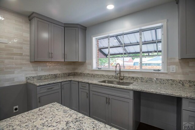 kitchen featuring light stone countertops, tasteful backsplash, a sink, and gray cabinetry