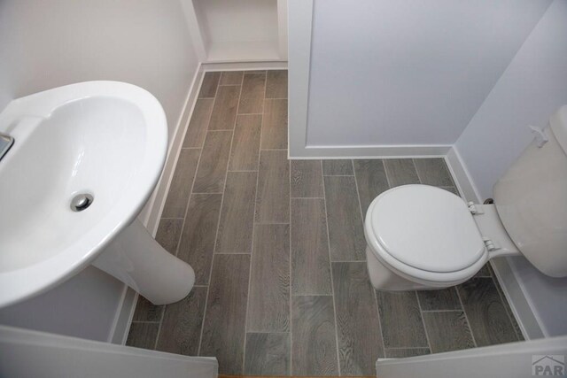 half bath featuring wood finish floors, a sink, toilet, and baseboards