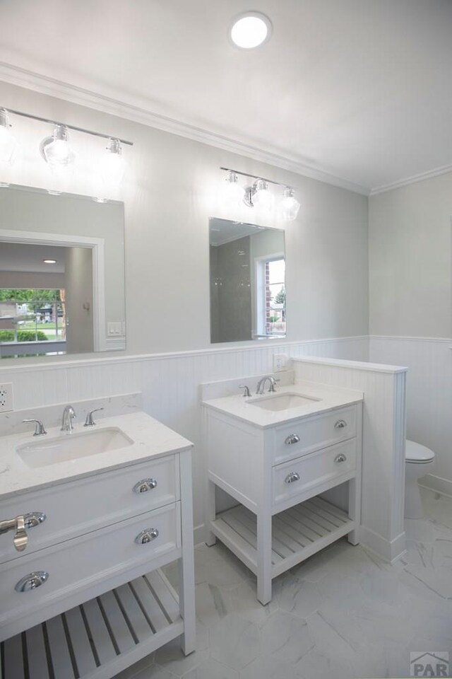 bathroom with marble finish floor, a wainscoted wall, toilet, ornamental molding, and a sink