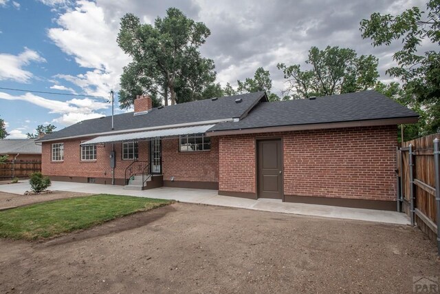 back of property with brick siding, fence, roof with shingles, a chimney, and a patio area