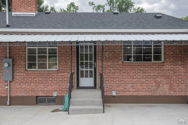 doorway to property featuring brick siding, a chimney, and roof with shingles