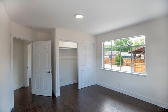 unfurnished bedroom with a closet, baseboards, and dark wood-style flooring