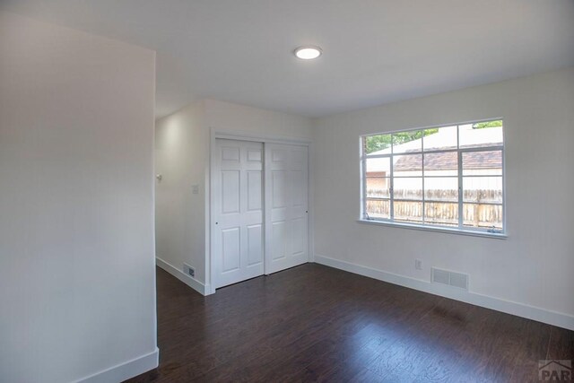 unfurnished bedroom featuring a closet, dark wood finished floors, visible vents, and baseboards