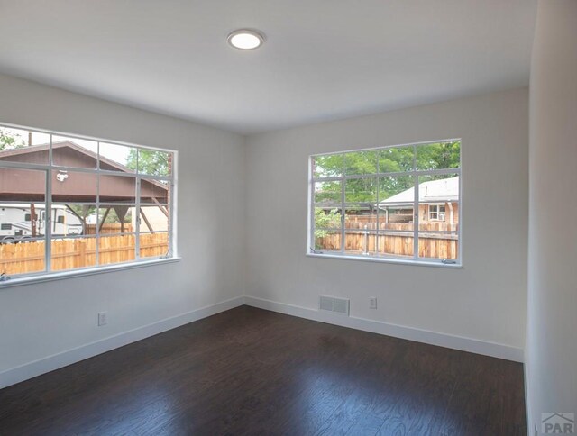 empty room featuring dark wood-style floors, visible vents, and baseboards