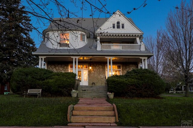 view of front facade featuring a balcony, stone siding, a porch, and a front yard