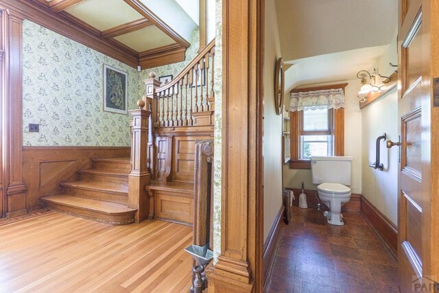 stairway featuring wood finished floors, a wainscoted wall, baseboards, and wallpapered walls