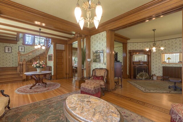 living area featuring a chandelier, a fireplace, stairs, ornamental molding, and wallpapered walls