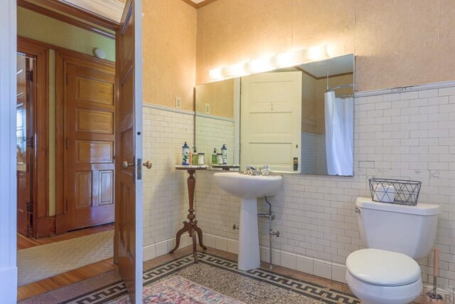 full bath featuring toilet, a wainscoted wall, tile walls, and a shower with curtain