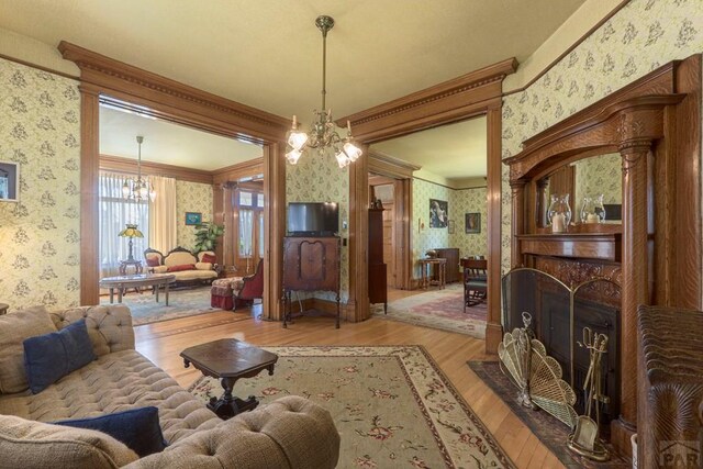 living area featuring a fireplace with flush hearth, a notable chandelier, ornamental molding, and wallpapered walls