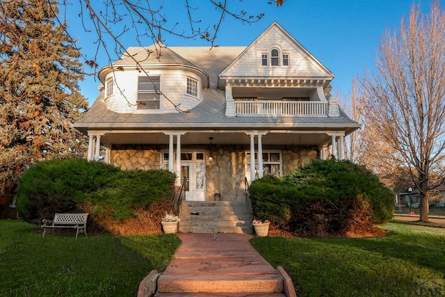 view of front of property featuring stone siding, a front lawn, and a balcony