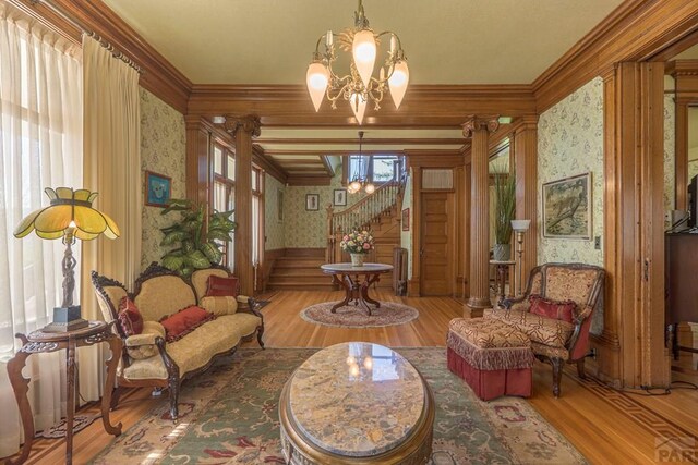 living area with crown molding, wallpapered walls, an inviting chandelier, wood finished floors, and stairs