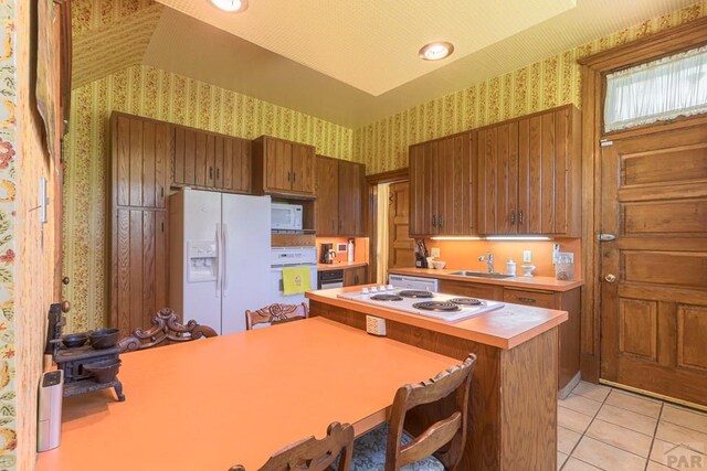 kitchen with light countertops, brown cabinetry, a sink, white appliances, and wallpapered walls