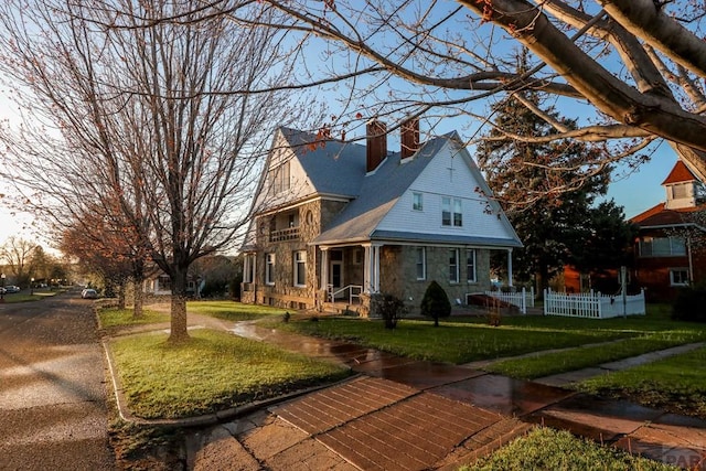 view of front facade featuring stone siding, a chimney, fence, and a front lawn