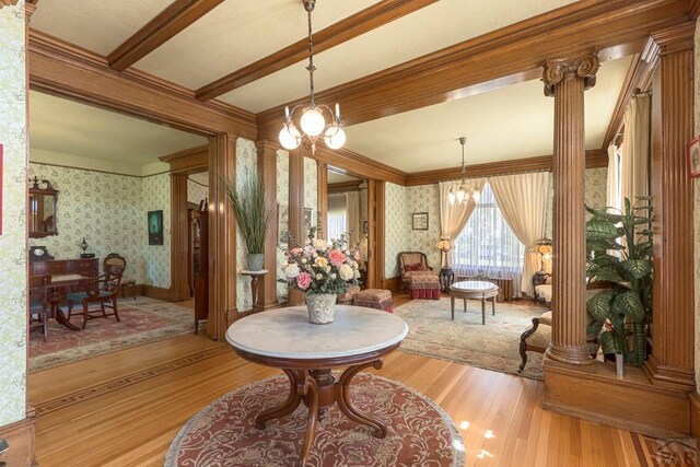 dining space with ornate columns, an inviting chandelier, light wood-style flooring, and wallpapered walls