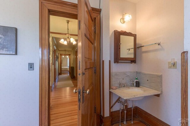 hallway with a chandelier, a sink, wood finished floors, and baseboards