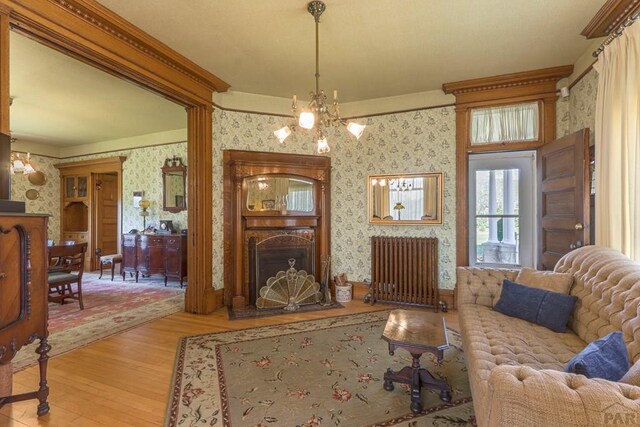 living room featuring a chandelier, light wood-style flooring, a fireplace, radiator heating unit, and wallpapered walls