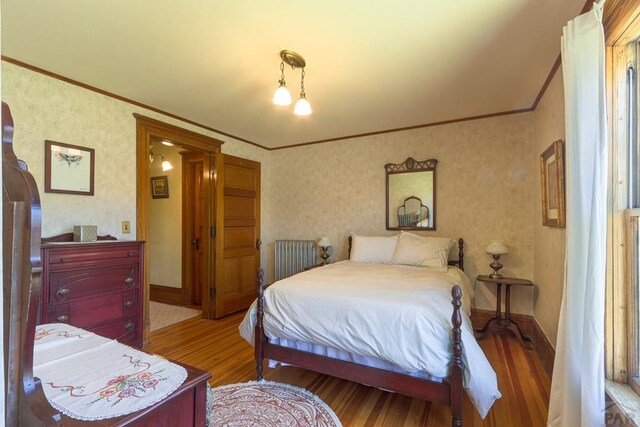 bedroom featuring radiator heating unit, crown molding, baseboards, and wood finished floors