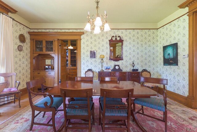 dining space featuring wallpapered walls, baseboards, wood finished floors, and an inviting chandelier