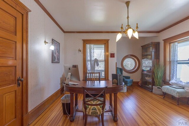 dining area with light wood-style floors, crown molding, a wealth of natural light, and an inviting chandelier