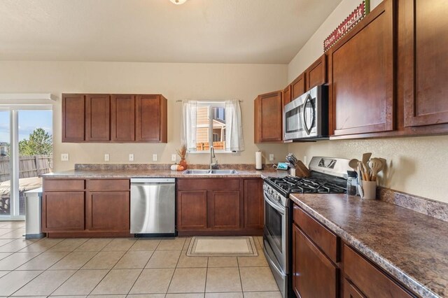 kitchen featuring appliances with stainless steel finishes, dark countertops, light tile patterned flooring, and a sink