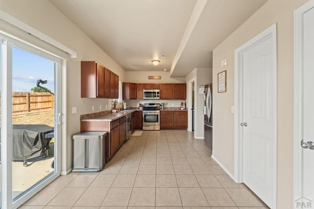 kitchen featuring light countertops, appliances with stainless steel finishes, light tile patterned flooring, a sink, and baseboards