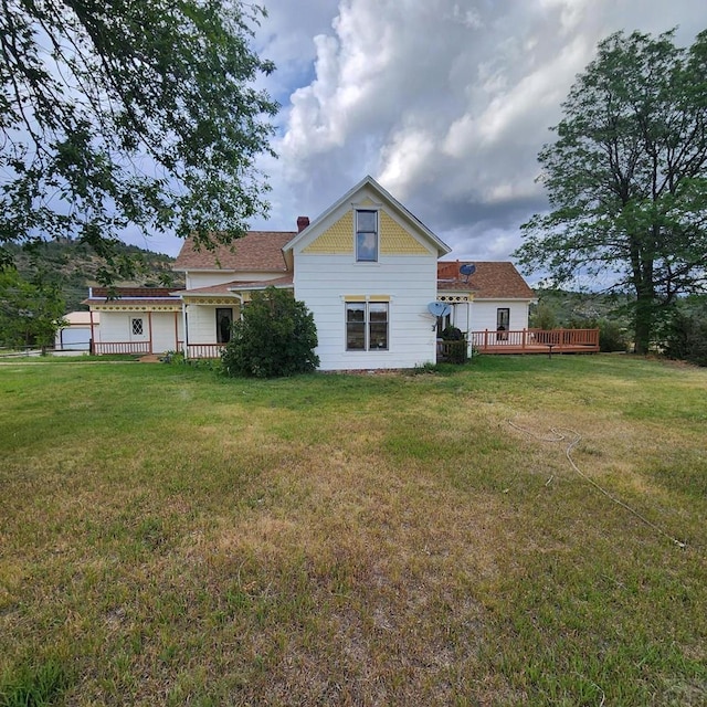 rear view of house featuring a lawn, a chimney, and a wooden deck