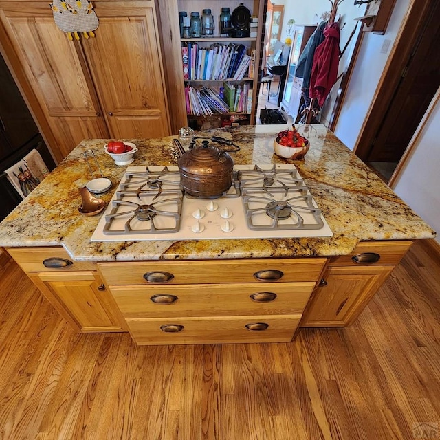 kitchen with light stone counters, light wood-type flooring, white gas cooktop, and brown cabinets