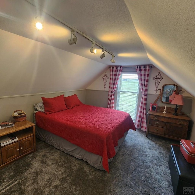 bedroom featuring lofted ceiling, dark carpet, and a textured ceiling