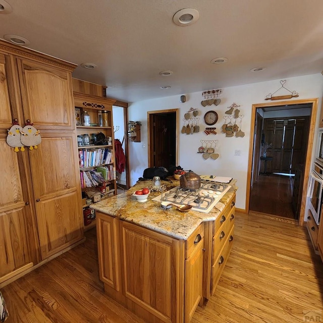 kitchen featuring light wood finished floors, white gas cooktop, a kitchen island, and light stone countertops