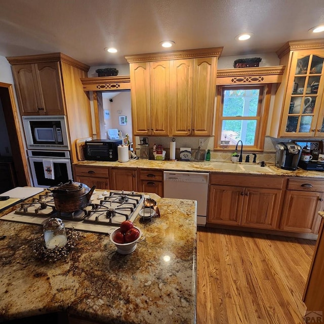 kitchen with white appliances, glass insert cabinets, light stone counters, light wood-type flooring, and a sink