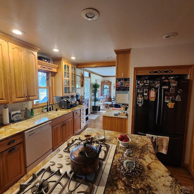 kitchen featuring recessed lighting, glass insert cabinets, a sink, light stone countertops, and white appliances