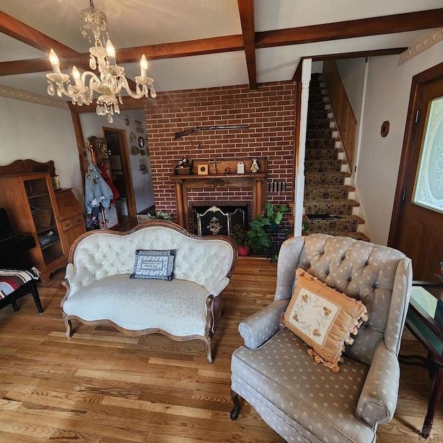 living area with wood finished floors, stairs, a brick fireplace, a chandelier, and beam ceiling