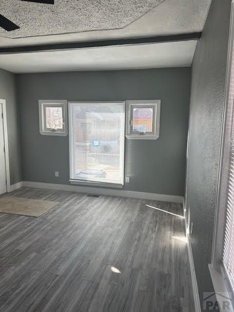 empty room featuring a textured ceiling, dark wood-type flooring, and baseboards