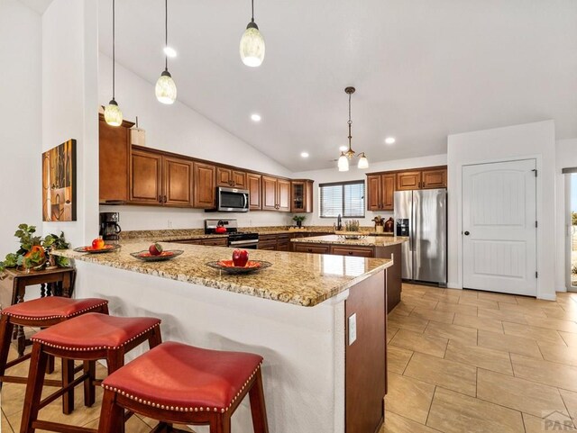 kitchen featuring a peninsula, light stone countertops, appliances with stainless steel finishes, and decorative light fixtures