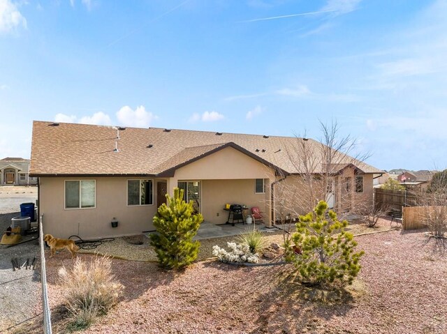 rear view of house featuring stucco siding, roof with shingles, fence, and a patio