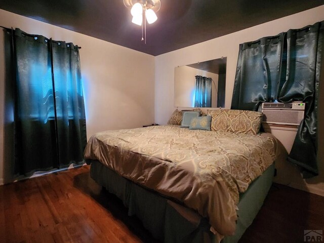 bedroom featuring dark wood-style floors, a ceiling fan, and cooling unit