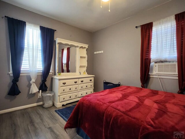 bedroom with cooling unit, baseboards, and wood finished floors