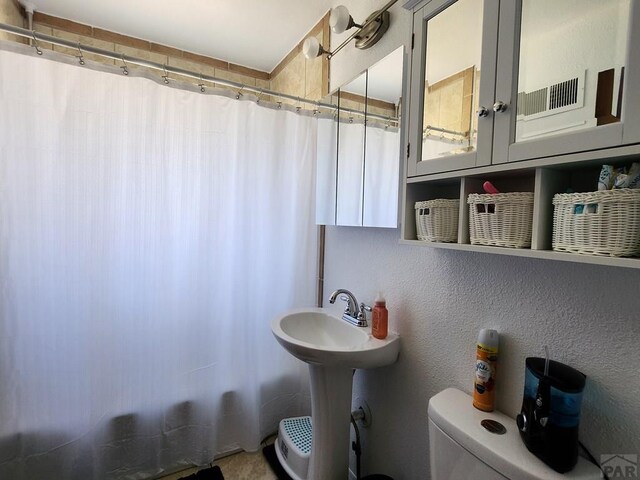 bathroom featuring toilet, a shower with curtain, and a textured wall